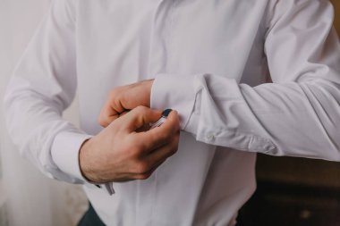 Bir adam beyaz gömlek giyiyor ve manşetlerini düzeltiyor. Formalite ve detaylara dikkat etme kavramı. Çünkü adam düzgün giyinmeye özen gösteriyor.