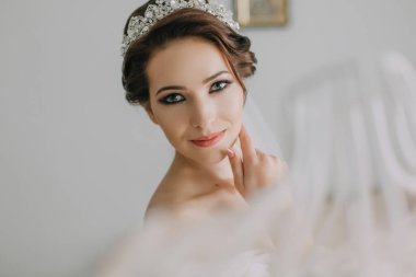 Kafasında taç ve saçında beyaz bir duvak olan bir kadın. Gülümsüyor ve kameraya bakıyor.