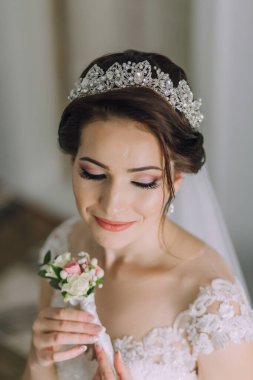 Bir gelin taç takıyor ve elinde çiçek tutuyor. Gelin düğününe hazırlanırken, zarafet ve kutlama kavramı. Elindeki çiçek sahneye doğal bir güzellik katıyor.