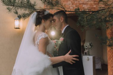 Bir gelin ve damat bir düğün töreninde birbirlerini kucaklıyorlar. Damat siyah bir takım giyerken gelin beyaz bir elbise ve duvak takıyor. Sahne samimi ve romantik.