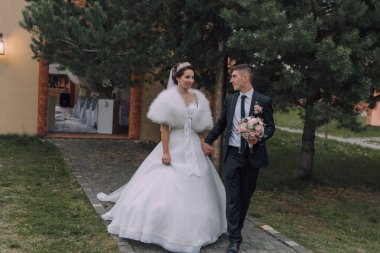 Bir gelin ve damat yolda yürüyor, gelin beyaz bir elbise giyiyor ve damat siyah bir takım elbise giyiyor.