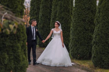 Bir gelin ve damat ormanda bir patikada yürüyorlar. Gelin beyaz bir elbise giyiyor ve damat da takım elbise giyiyor.