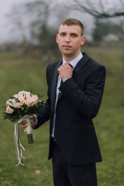 Takım elbiseli ve kravatlı bir adam elinde bir buket çiçekle bir tarlada duruyor. Zarafet ve entelektüellik anlayışı, çünkü adam resmi giyinmiş.