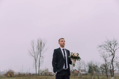 Takım elbiseli ve kravatlı bir adam elinde bir buket çiçekle bir tarlada duruyor. Sahne sessiz ve huzurlu, adam uzaklığa bakıyor. Buketteki çiçekler beyaz ve pembe.