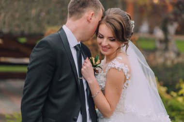 Bir gelin ve damat birbirlerine sarılıp öpüşüyorlar. Gelin beyaz bir elbise giyiyor ve damat siyah bir takım giyiyor.