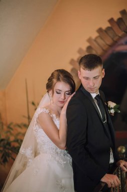 Bir gelin ve damat düğün fotoğrafında birbirlerine sarılıyorlar. Gelin beyaz bir elbise giyiyor ve damat siyah bir takım elbise giyiyor. Fotoğrafın sıcak ve romantik bir havası var.