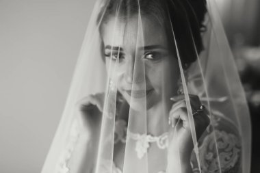 Bir gelin peçe takıyor ve kameraya bakıyor. Gülümsüyor ve mutlu.