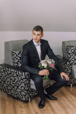 Takım elbiseli ve papyonlu bir adam elinde bir buket çiçekle bir sandalyeye oturur. Zarafet ve entelektüellik anlayışı, çünkü adam resmi giyinmiş.