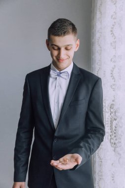 Takım elbiseli ve kravatlı bir adam elinde bir yüzük tutuyor. Gülümsüyor ve mutlu.