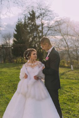 Gelin ve damat tarlada, gelinle birlikte beyaz bir elbise ve kürk şalla dikiliyorlar.