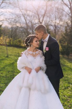 Gelin ve damat bir tarlada, gelinle birlikte beyaz kürk manto giyiyorlar. Damat gelini yanağından öpüyor.