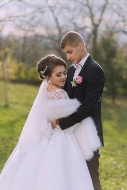 Bir gelin ve damat tarlada fotoğraf çektirmek için poz veriyorlar. Gelin beyaz bir elbise giyiyor ve damat bir takım elbise giyiyor. İkisi de gülümsüyor ve mutlu görünüyorlar. Aşk ve mutluluk kavramı