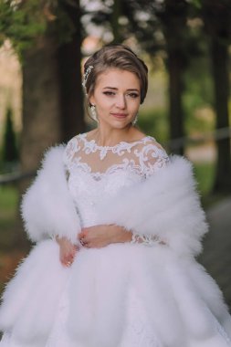 Beyaz elbiseli bir kadın beyaz kürk şort giyiyor. Gülümsüyor ve kameraya bakıyor.