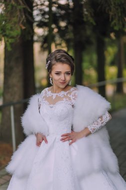 Beyaz elbiseli bir kadın beyaz kürklü bir resim için poz veriyor. O bir çift küpe ve bir kolye takıyor. Görüntünün sıcak ve zarif bir havası var. Kadının kendine güveni tam.