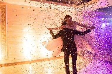 Konfetilerle çevrili bir adam ve kadın havada dans ediyorlar. Sahne kutlama ve neşe dolu, zira çift büyük olasılıkla düğün veya yıldönümü gibi özel bir olayı kutluyor.