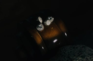 İçinde üç küpe olan tahta bir kutu. Küpeler gümüş ve elmas şeklinde. Kutu karanlık bir odada bir masanın üzerinde.