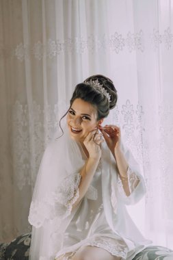 Bir kadın kanepede oturuyor ve gelinliğini giyiyor. Gülümsüyor ve kameraya bakıyor.