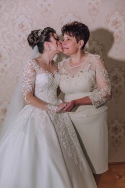 İki kadın birbirine sarılıyor, bir tanesi gelinlik giyiyor. Diğer kadın beyaz bir elbise giyiyor.