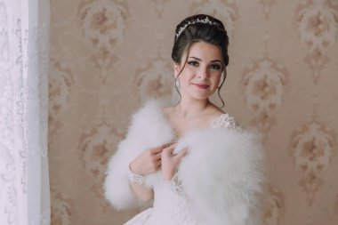 Beyaz kürk manto ve taç giyen bir kadın. Gülümsüyor ve kameraya bakıyor.