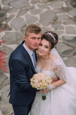 Bir gelin ve damat bir buket çiçekli fotoğraf için poz veriyorlar. Gelin beyaz bir elbise giyiyor ve damat mavi bir takım elbise giyiyor. Sahne mutlu ve kutlama dolu.