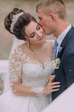 Bir gelin ve damat birbirlerinin dudaklarını öpüyor. Gelin beyaz bir elbise ve taç giyiyor. Damat mavi bir takım elbise giyiyor. Aşk ve mutluluk kavramı