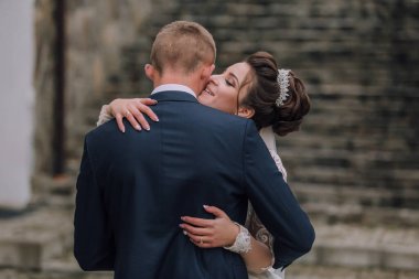 Bir erkek ve bir kadın birbirlerine sarılıyorlar. Takım elbiseli bir adam ve gelinlik giyen bir kadın.