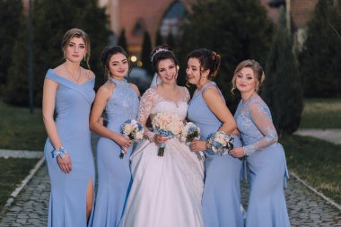 Bir gelin ve nedimeleri resim için poz veriyorlar. Gelin beyaz bir elbise giyiyor ve nedimeler mavi elbiseler giyiyor. Sahne mutlu ve kutlama dolu, gelin olarak.