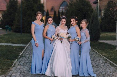 Bir grup kadın mavi elbiseli bir fotoğraf için poz veriyor. Kadınlardan biri beyaz bir elbise giyiyor ve elinde bir buket çiçek tutuyor. Fotoğrafın sıcak ve dostane bir havası var.