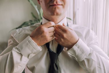 Bir adam siyah kravat takmaya hazırlanıyor. Gülümsüyor ve keyfi yerinde.