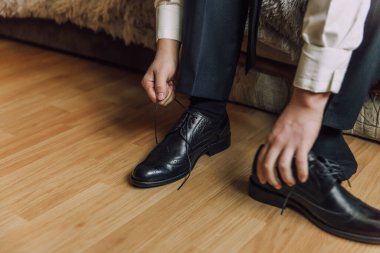 Bir adam ayakkabılarını giymeye hazırlanıyor. Siyah bir ayakkabı ve mavi bir takım elbise giyiyor.