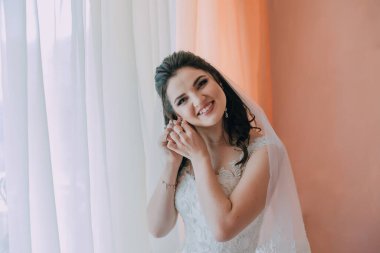 Bir kadın düğünü için hazırlanıyor ve duvağını takıyor. Gülümsüyor ve kameraya bakıyor.