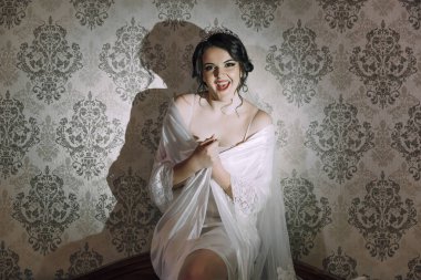 Beyaz elbiseli bir kadın sandalyede oturuyor. Kolye ve taç takıyor.