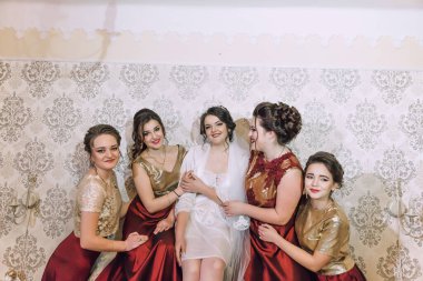 Beş kadından oluşan bir grup, ortasında bir gelin olan bir fotoğraf için poz veriyor. Gelin beyaz bir elbise giyiyor ve arkadaşları tarafından çevrili. Sahne mutlu ve kutlama dolu.