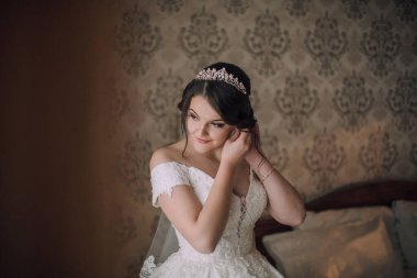 Bir kadın düğün için hazırlanıyor ve tacını takıyor. Görüntünün klasik bir havası var. Yatakta oturan kadın ve yıpranmış bir görünüşü var.