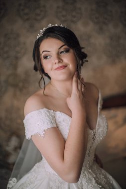 Beyaz elbiseli bir kadın gülümsüyor ve kameraya bakıyor. O bir taç takıyor ve eli yüzünde.