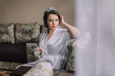 Beyaz bornozlu bir kadın elleri kucağında kanepede oturuyor. O bir taç takıyor ve küçük beyaz bir çiçek tutuyor. Sahne samimi ve huzurlu.