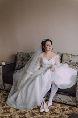 Gelinlikle kanepede oturan bir gelin. Beyaz bir elbise ve duvak takıyor.