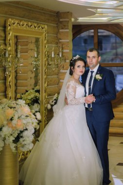 Bir gelin ve damat aynanın önünde fotoğraf için poz veriyorlar. Gelin beyaz bir elbise giyiyor ve damat mavi bir takım elbise giyiyor. Sahne mutlu ve kutlama dolu.