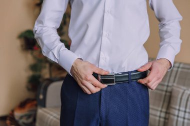 Beyaz gömlekli ve mavi pantolonlu bir adam kemerini ayarlıyor. Formalite ve detaylara dikkat etme kavramı. Çünkü adam kemerinin düzgün bağlandığından emin olmak istiyor.