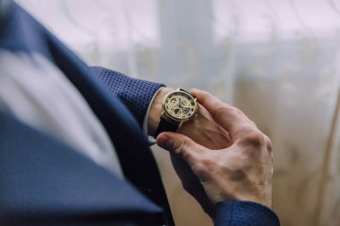 Bir adam altın bir saat takıyor ve yüzüne doğrultuyor. Saat sol bileğinde.