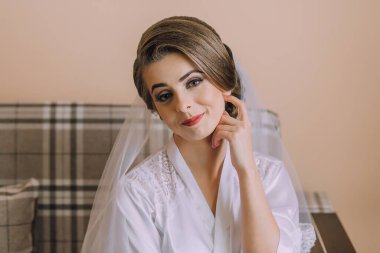 Beyaz cüppeli bir kadın kanepede oturuyor. Bir peçe takıyor ve eli yüzünde.