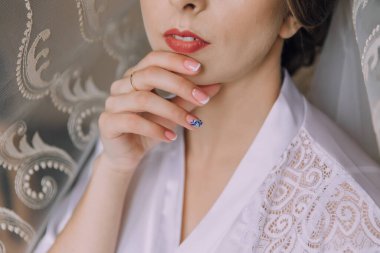 Mavi tırnak cilası ve kırmızı dudağı olan bir kadın beyaz bir bornoz giyiyor. O, ellerine bakıyor.