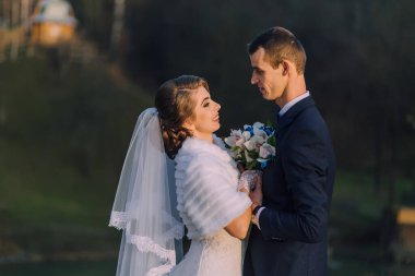 Gelin ve damat bir arada duruyorlar, gelin bir buket tutuyor ve damat vazo tutuyor.