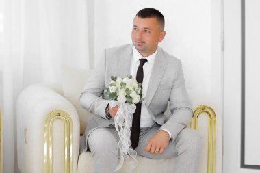 Takım elbiseli ve kravatlı bir adam elinde bir buket çiçekle kanepede oturur. Zarafet ve entelektüellik anlayışı, çünkü adam resmi giyinmiş.