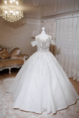 Üzerinde bir sürü parıltı olan beyaz bir elbise bir odada sergilenir. Elbise bir mankenin üzerinde ve ilgi odağı. Odada çok ışık var.