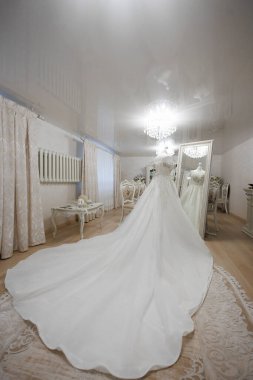 Bir gelin büyük aynalı bir odada düğününe hazırlanıyor. Oda beyaz perdeler ve mobilyalarla dekore edilmiş, temiz ve zarif bir atmosfer sağlıyor.