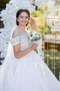 Beyaz elbiseli bir kadın elinde bir buket çiçek tutuyor. Gülümsüyor ve mutlu.