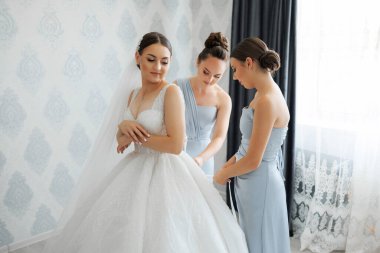 Bir gelin nedimeleriyle düğününe hazırlanıyor. Gelin beyaz bir elbise giyiyor ve nedimeler mavi elbiseler giyiyor. Sahne mutlu ve kutlama dolu.