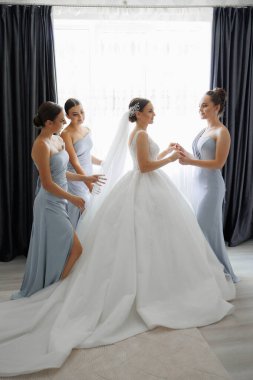 Bir gelin nedimeleriyle düğününe hazırlanıyor. Gelin beyaz bir elbise giyiyor ve nedimeler mavi elbiseler giyiyor.