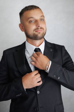 Takım elbiseli ve kravatlı bir adam kravatını bağlamaya hazırlanıyor. Gülümsüyor ve keyfi yerinde.